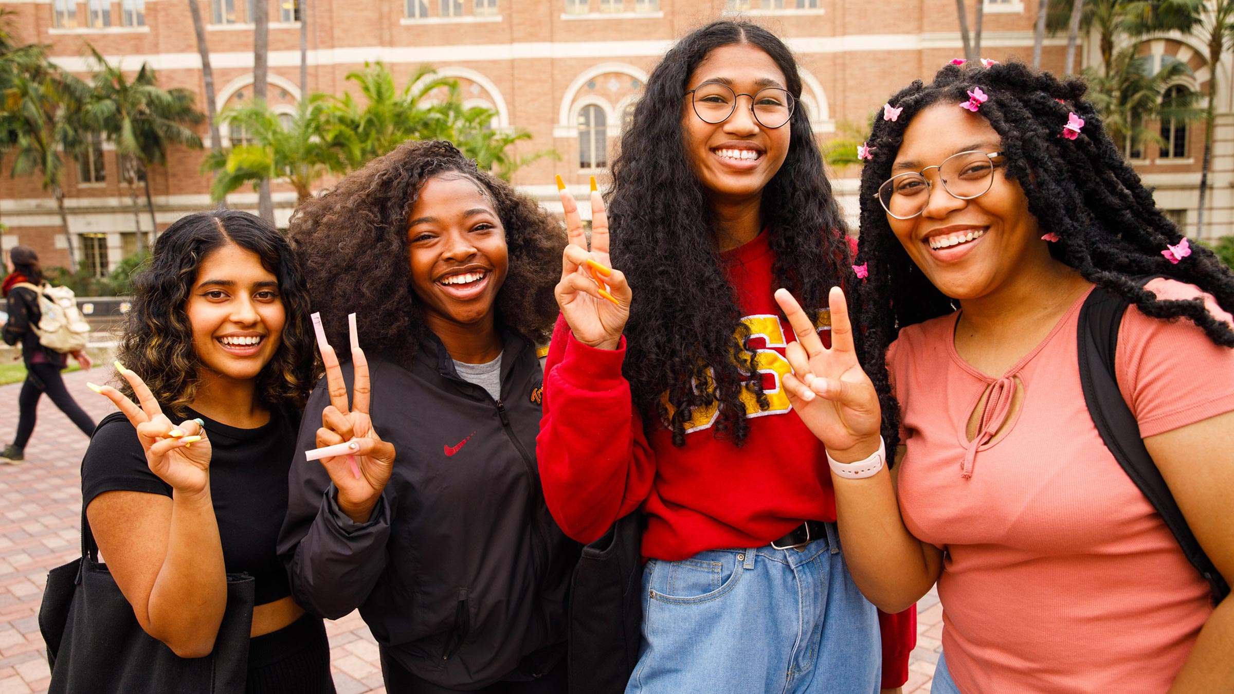 Four students holding up "Fight On" hand sign and smiling wearing USC branded merch.